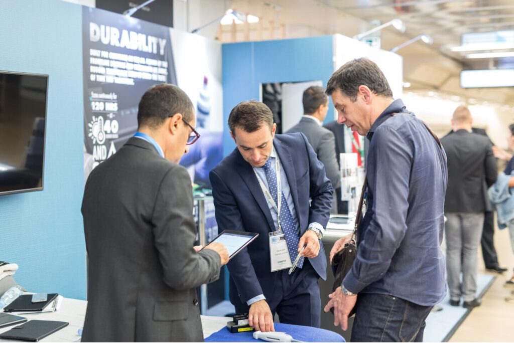 Three men at a booth at a trade show exchanging information.