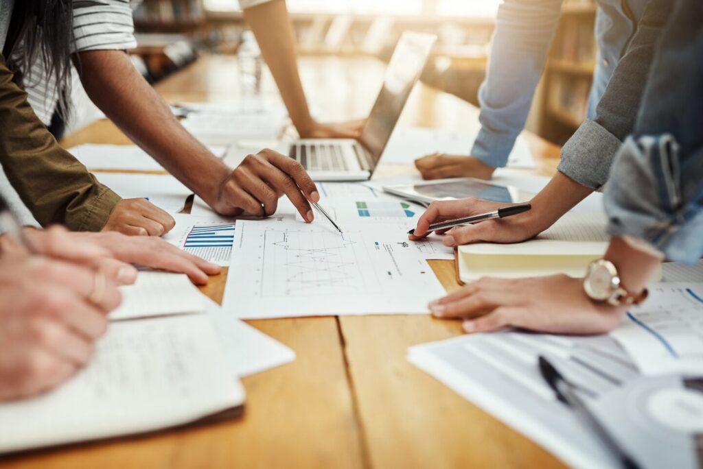 A group of people working over a table filled with graphs and charts,
