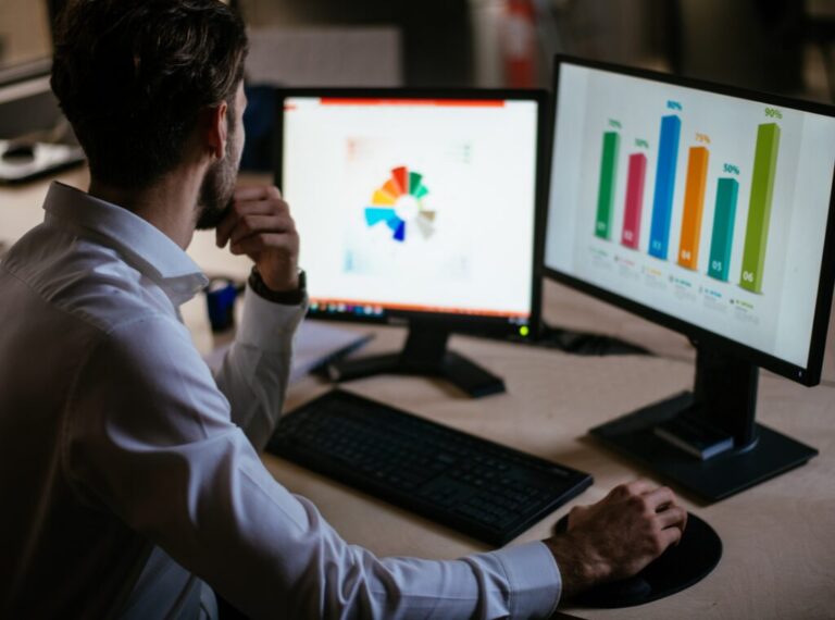 Man at desk looking over pie charts and data graphs on his computer.