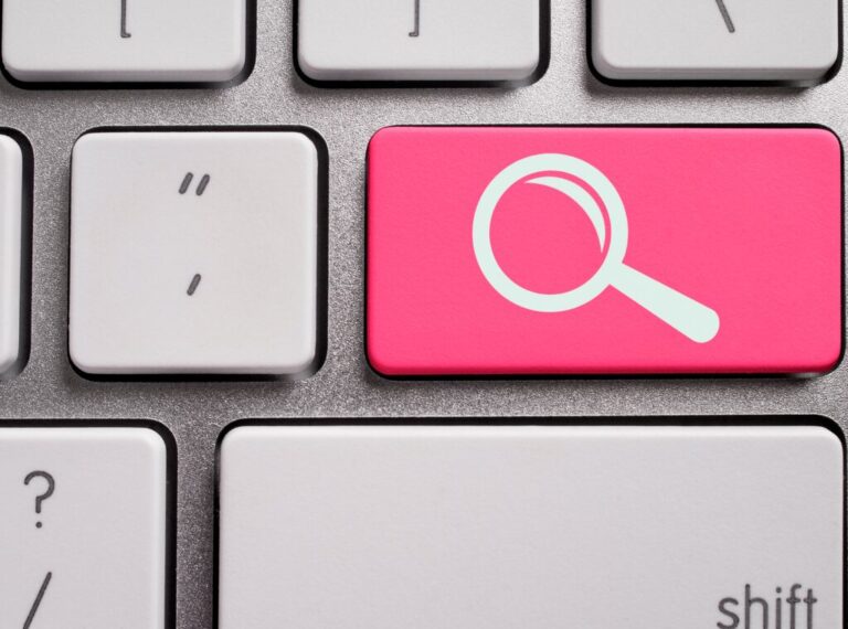 Computer keyboard with a button that has the image of a magnifying glass on it representing 'Search'.