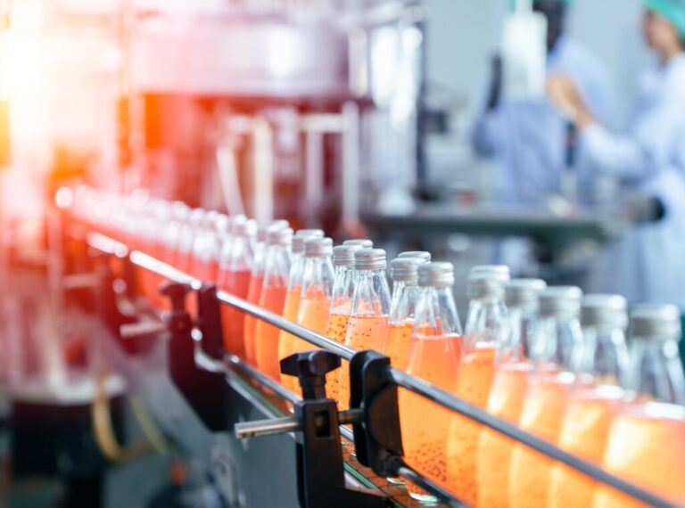 A manufacturing belt with dozens of bottles with orange liquid passing out of frame.