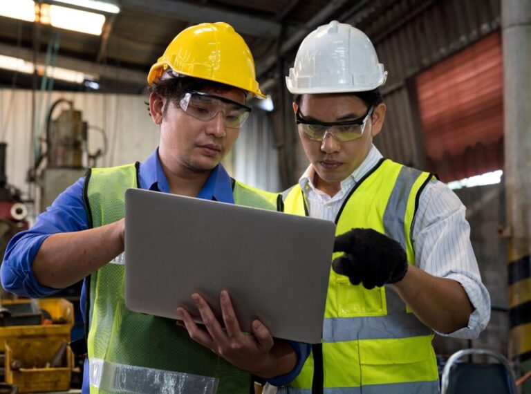 Two manufacturing workers in protective gear looking at a laptop.