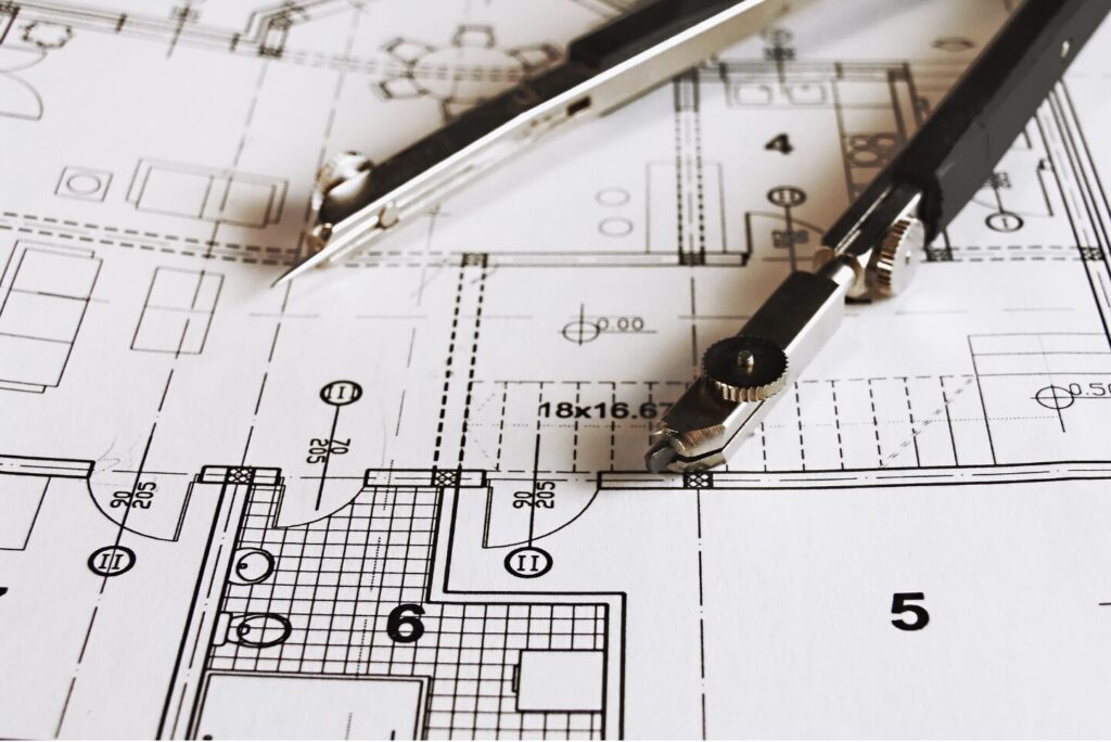 Architectual plans laid out on a table with a drawing compass on top.