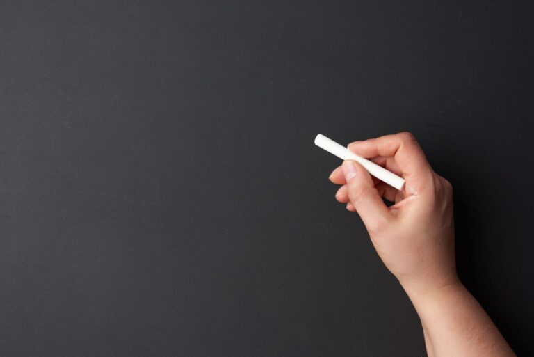 Hand holding a piece of Chaulk about to write on a blackboard.