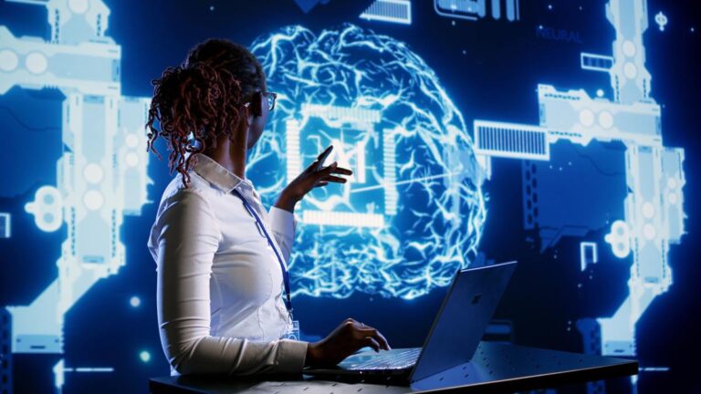 AI expert on laptop pointing at blue graphic of brain with "AI" in the middle