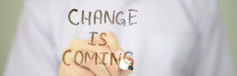 Business person writing “Change Is Coming” with marker on a clear board