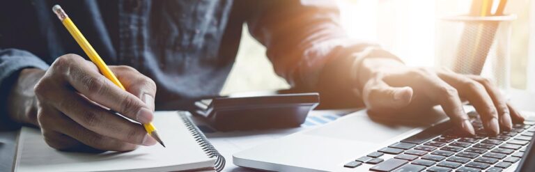 man writing in a notebook with hand on laptop keyboard