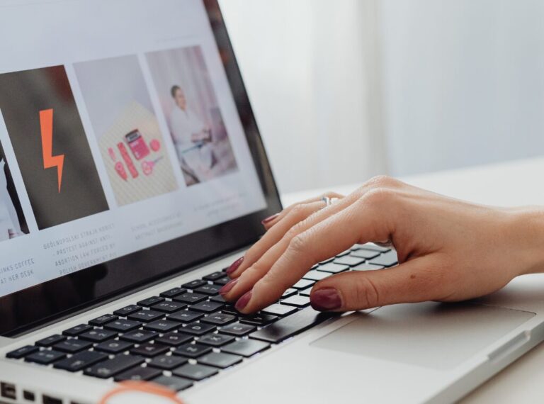 woman with bright red nails typing on a laptop with a business website open.